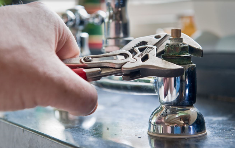 Close-up of a hand holding a wrench, using it on a sink fixture.