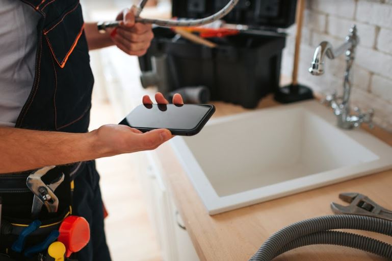 Plumber using phone while repairing a sink in a home.