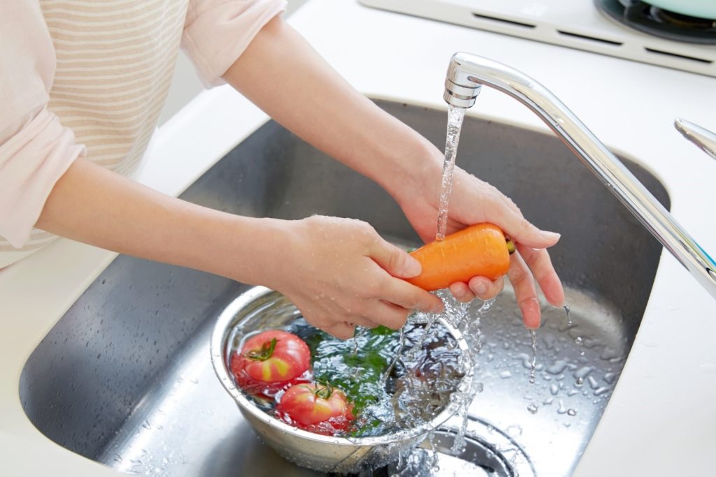 Woman's hands washing vegetables in a kitchen sink.