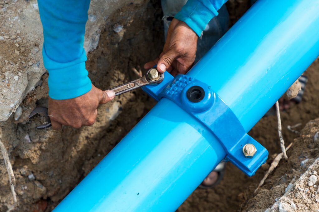 Man using a large wrench on water pipes. Construction site with new Water Pipes in the ground
